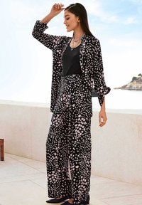 Schwarzes Outfit mit einer langärmligen Druckjacke und weit geschnittenen Hosen mit einem rosa gepunkteten Muster. Glattes Material und entspannte Passform.