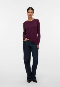 Paars langemouwtop met een ronde hals, gecombineerd met donkerblauwe rechte jeans. De stof lijkt zacht met een gladde textuur.
