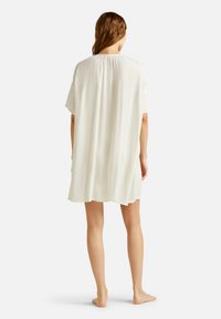 Vestido corto blanco, plisado, con un corte holgado, mangas cortas y un escote redondeado, que presenta una textura suave y ligera.