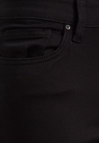 Vaqueros de mezclilla negra con una textura suave, que presentan un diseño de bolsillo estándar y un pequeño detalle de botón metálico.