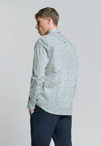 Hellblau gemustertes Hemd mit kleinen, mehrfarbigen Punkten, langen Ärmeln und einem klassischen Kragen. Verfügt über einen Knopf am Nacken hinten.