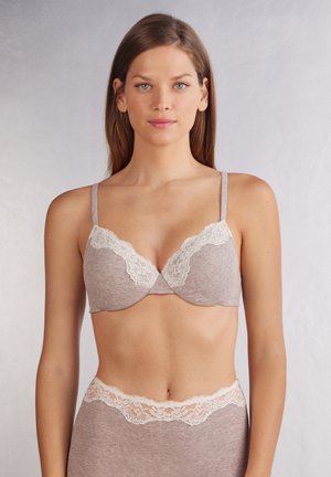 Bra with light brown ribbed fabric, lace trim at the cup edges, adjustable straps, and a smooth, rounded shape. Simple design with no embellishments.