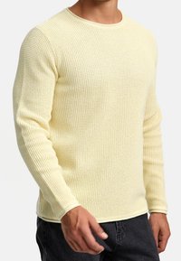 Pull tricoté jaune clair avec un motif texturé et un col rond, doté de manches longues et de poignets côtelés.