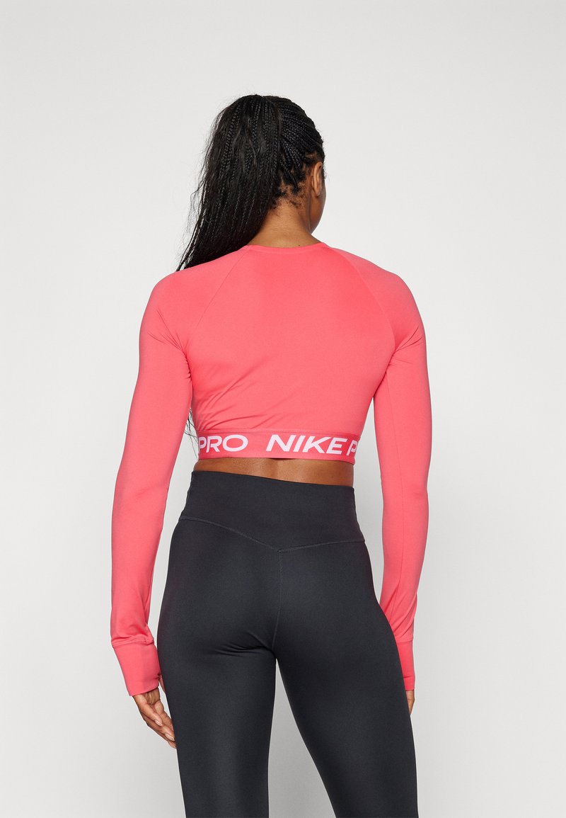 Długi rękaw, skrócona bluzka do ćwiczeń w jaskrawym różowym kolorze, z białą, elastyczną taśmą z logo w talii oraz gładkim, rozciągliwym materiałem. Czarne legginsy z wysokim stanem.