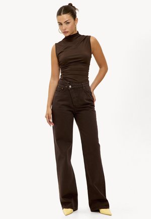 Haut marron sans manches avec un col montant et un effet froncé, associé à un jean large taille haute marron foncé et des talons jaunes à bout pointu.