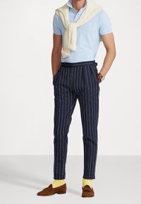 Světle modrá polo tričko s pleteným krémovým svetrem přehozeným přes ramena, spárované s námořnickými proužkovými kalhotami a hnědými mokasíny.