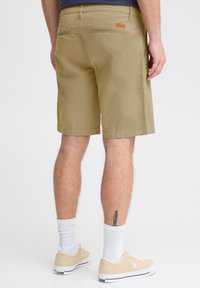 Licht khaki shorts met een reguliere pasvorm, gekarakteriseerd door een gladde textuur, zijzakken en een achterzakdetail. Gecombineerd met beige sneakers en witte sokken.