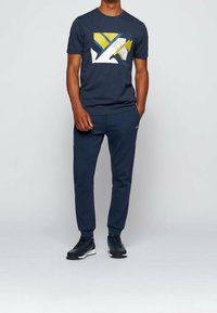 En marinblå sportoutfit bestående av en t-shirt med rund hals och geometriskt mönster samt matchande avsmalnande sweatpants, båda gjorda av mjukt material.