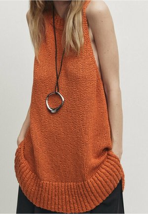 Knit orange sleeveless top with a ribbed hem, featuring a loose fit and pockets; paired with a black necklace and worn over dark pants.