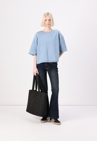 Τζιν φανέλα σε ανοιχτό μπλε χρώμα, φαρδιά σκούρα τζιν και μαύρη τσάντα tote. Διαθέτει φαρδιά μανίκια και ορατές ραφές. Μαύρα αθλητικά παπούτσια με μπεζ σόλες.