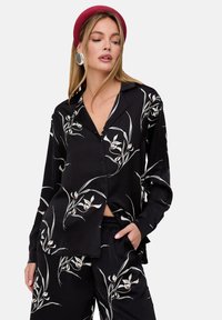 Black long-sleeve shirt with white floral print, buttoned front, and collar. Paired with matching pants, featuring a relaxed fit.