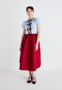 Blå cropped topp med pufferslag og svart blomsterbroderi, sammen med et langt rødt skjørt med blomster mønster. Svarte sko med stropper.
