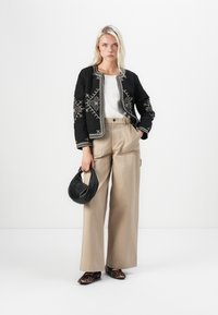 Quilted black jacket with white embroidery, cream top, beige wide-leg pants, black bag, and leopard print shoes. Smooth textures, structured fit.