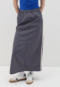 Grijze, lange rok van lichtgewicht stof met een elastische tailleband en zijsplitten, gecombineerd met witte en beige sneakers.