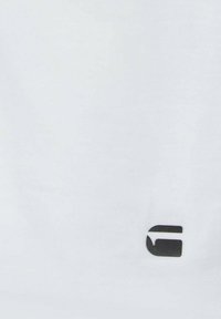 Weißer Stoff mit einem kleinen, schwarz stilisierten Buchstaben "G", der in der Nähe der unteren rechten Ecke gedruckt ist.