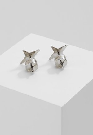 Paar zilveren oorknopjes in stervorm met schroefsluiting, geplaatst op een witte schuine ondergrond.