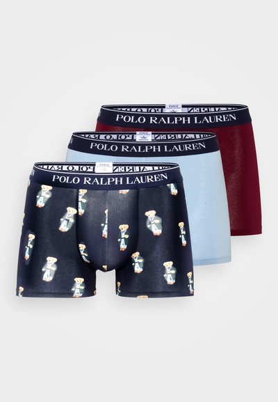 Três pares de boxers masculinos: preto com estampa de urso de peluche, azul claro e bordô. Todos têm uma cintura com marca. Material em algodão.