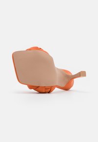 Chaussure à talon haut orange avec une semelle texturée, présentant un design élégant et une bride étroite, mettant en valeur un matériau synthétique lisse.