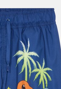 Shorts de bain bleus avec une taille élastique, ornés de motifs de palmiers verts et orange. Tissu doux au toucher lisse.