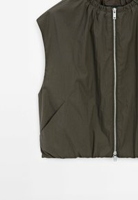 Veste sans manches vert olive avec une fermeture éclair argentée à l'avant et des poches latérales inclinées, en tissu léger froissé.