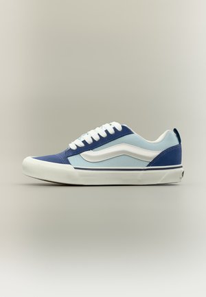 Χαμηλό sneaker σε μπλε και ανοιχτό μπλε με λευκή πλευρική ρίγα, λευκά κορδόνια και λευκή καουτσούκ σόλα σε ουδέτερο φόντο.