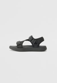 Svart sandaler med justerbare stropper, laget av stoff og gummi. Har en flat såle og åpen design for fotventilasjon.