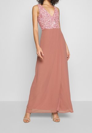 Mujer con vestido rosa sin mangas, corpiño con lentejuelas y falda de gasa fluida, combinada con sandalias de tacón alto color nude.