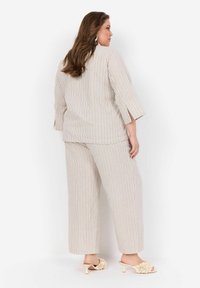 Lys beige stribet dragt med trekvartærmer og brede ben. Accentueret med subtile, farverige linjer; parret med lyse blomstrede hæl-sandaler.