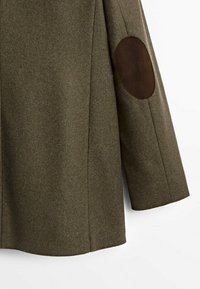 Manteau en laine vert olive à coupe droite, comportant des coudières en cuir marron et un tissu texturé, offrant un contraste de matériaux.