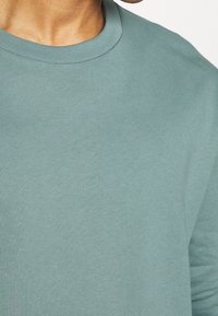 Helle teal Crewneck-Sweatshirt mit glatter Textur und geripptem Kragen. Der Stoff ist weich und hat eine lockere Passform.