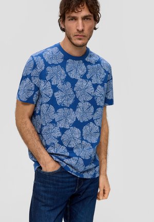 Blauw T-shirt met korte mouwen met een groot, wit bladpatroon. Zachte textuur met een ronde hals, gecombineerd met donkerblauwe jeans.