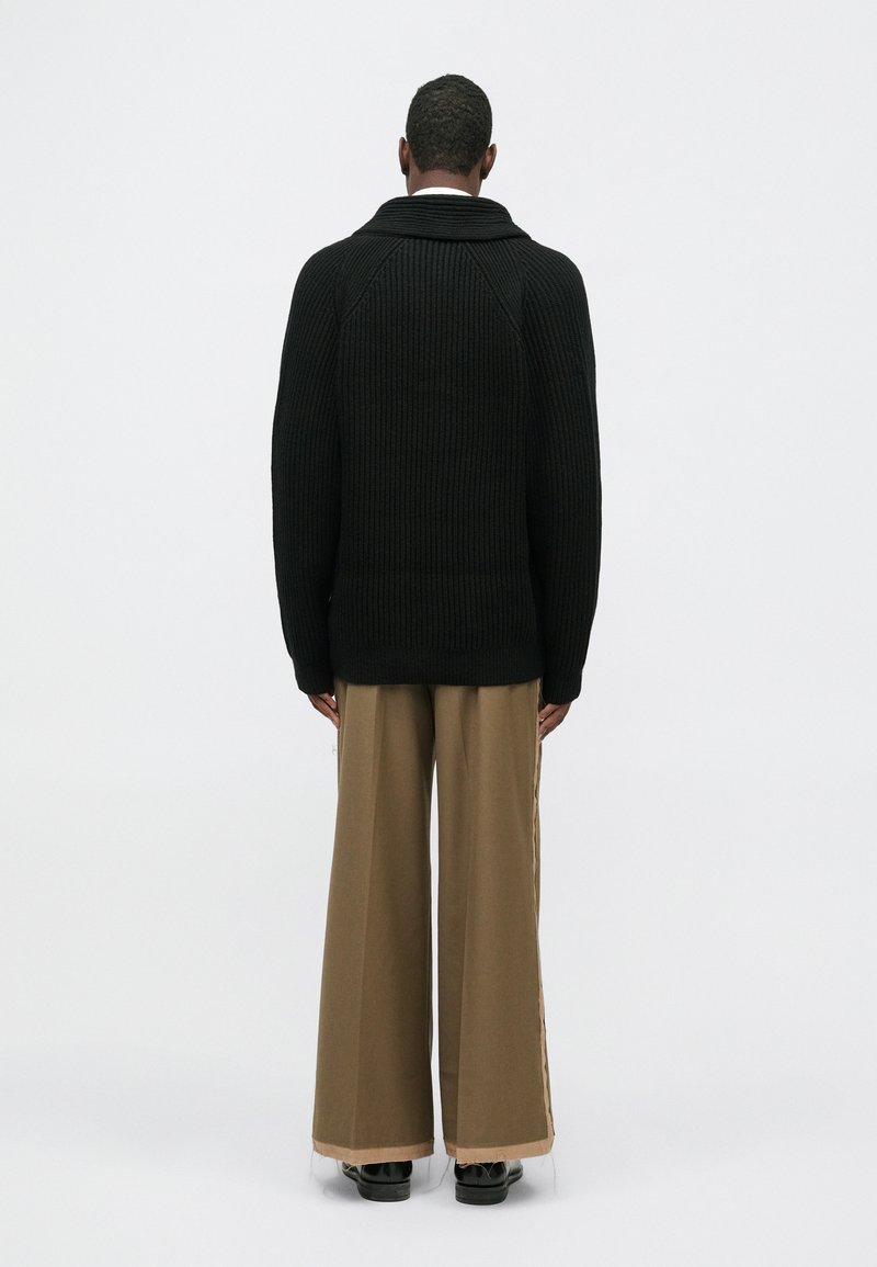 Maglione nero a coste con un ampio colletto, abbinato a pantaloni larghi di colore beige. L'outfit presenta una finitura texturizzata e un taglio rilassato.