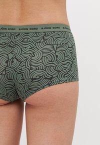 Sous-vêtements verts à motifs avec un design de vagues. Dotés d'une ceinture élastique noire avec le logo "BJÖRN BORG". Fabriqués en matériau doux et extensible.