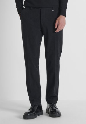 Zwarte op maat gemaakte broek met een gladde textuur, rechte pasvorm en subtiele voormessen; gedragen met zwarte veterschoenen.