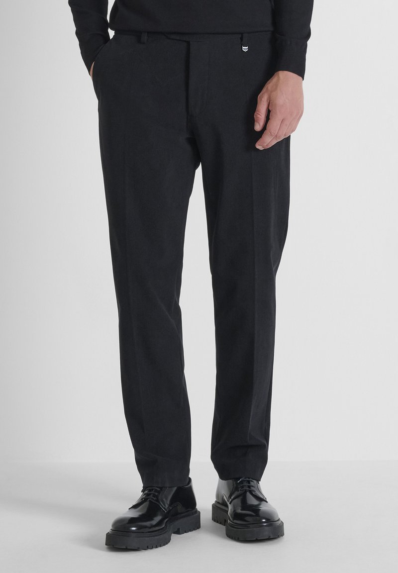 Zwarte op maat gemaakte broek met een gladde textuur, rechte pasvorm en subtiele voormessen; gedragen met zwarte veterschoenen.