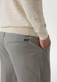 Light beige sweater and gray pants featuring a back pocket with a black "GUESS" label. The fabric appears textured and casual.