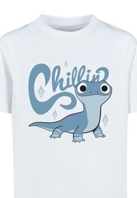Vit t-shirt med en illustrerad blå dinosauriekaraktär med stora ögon och texten "Chillin'" i ett lekfullt typsnitt, prydd med diamanter.