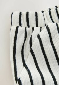 Tissu en coton blanc avec des rayures verticales noires, présentant une surface texturée et côtelée. Les bords pliés avec une finition élastique sont affichés.