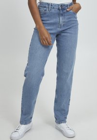 Jeans de tiro alto de color azul claro hechos de mezclilla. Cuentan con pierna recta, pasadores para cinturón, bolsillos delanteros y un cierre de cremallera con botón.