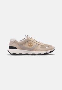 Chaussure de sport beige en cuir et textile mélangés, semelle amortissante et semelle extérieure en caoutchouc noir. Présente un détail de logo sur le côté.
