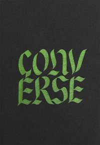 Černá tkanina se výrazným, stylizovaným textem "CONVERSE" v jasně zelené barvě. Design má různorodé tvary písmen a texturovaný vzhled.
