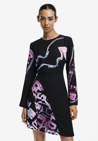 Schwarzes Kleid mit langen Ärmeln, das abstrakte pinke und blaue Muster aufweist. Der strukturierte Stoff und der asymmetrische Saum verleihen visuelles Interesse.