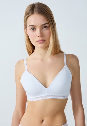 Bralette blanche avec de fines bretelles ajustables, décolleté en V et bordure en dentelle le long du bas. Texture lisse. Design simple et minimaliste.