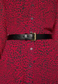 Robe rouge et noire à imprimé léopard avec des boutons noirs sur le devant, cintrée à la taille par une ceinture en cuir noire à boucle rectangulaire dorée.
