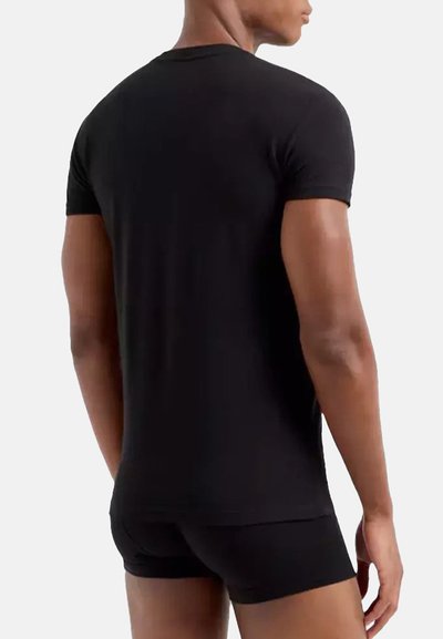 T-shirt nera a maniche corte realizzata in tessuto morbido, con scollatura rotonda e silhouette aderente. Indossato con pantaloni corti neri abbinati.