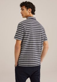 Kratkām piedurknēm polo krekls tumši zilā krāsā ar baltām horizontālām svītrām. Tam ir klasisks apkakle un brīvs piegriezums ar smalku tekstūru.