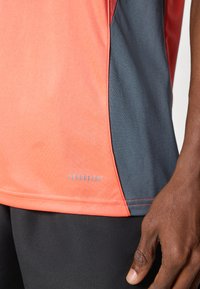 Aeroready sportshirt met een combinatie van koraal en donkergrijze materialen, met een soepel textuur en contrasterende zijpanelen.