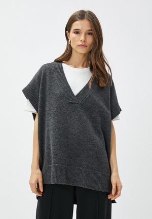 Gilet en tricot gris surdimensionné avec un col en V, des détails côtelés et des manches courtes, superposé sur un t-shirt à col rond blanc.