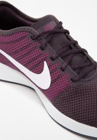 Lila och svart sportskor med ett ventilerande mesh-övre, som har en vit Nike-logotyp, texturerade detaljer och en vit sula.