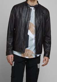 Zwarte lederen motorjack met een ronde kraag, ritszak en een gladde textuur, gelaagd over een gestreept shirt en cargobroek.